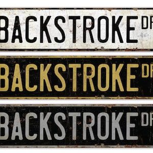 May include: Three vintage-style metal signs with the text "BACKSTROKE DR" in black, gold, and silver lettering on a black background.
