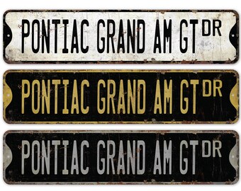 May include: Three vintage-style metal signs with the text "PONTIAC GRAND AM GT DR" in black, gold, and silver lettering on a black background.