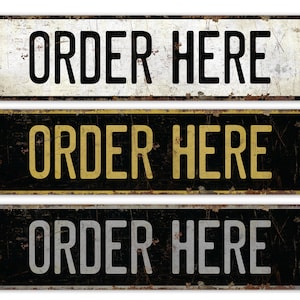 Op de afbeelding: Drie vintage-stijl metalen borden met de tekst "ORDER HERE" in zwarte, gouden en zilveren letters op een zwarte achtergrond.