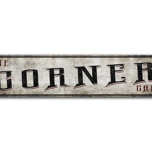 以下が含まれることがあります： 白く古びた金属製の看板で、黒い文字で「THE CORNER CAFE」と書かれています。