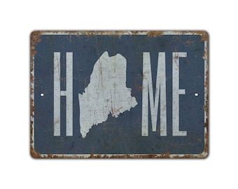 May include: A rectangular metal sign with a distressed finish. The sign is navy blue with the word "HOME" in white block letters. The shape of the state of Maine is in white in the centre. The edges of the sign are rusty.