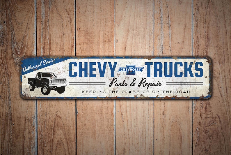 K&ouml;nnte beinhalten: Ein rechteckiges Metallschild mit abgenutztem Finish, das die Worte "CHEVY TRUCKS" in Blau und eine schwarze LKW-Illustration zeigt. Das Schild enth&auml;lt auch den Text "Parts & Repair" und "KEEPING THE CLASSICS ON THE ROAD."