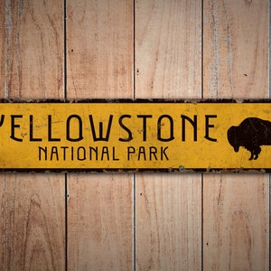 May include: Yellowstone National Park sign with a black silhouette of a buffalo on a yellow background with black lettering. The sign is made of metal and has a distressed look.