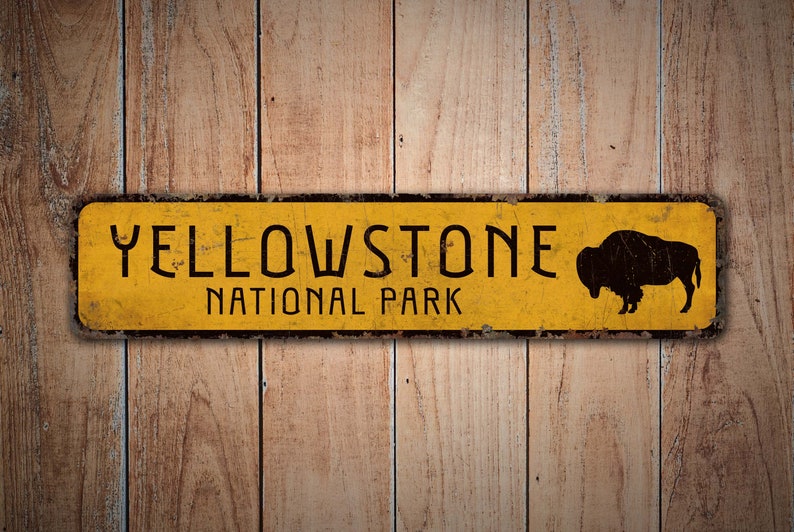 May include: Yellowstone National Park sign with a black silhouette of a buffalo on a yellow background with black lettering. The sign is made of metal and has a distressed look.