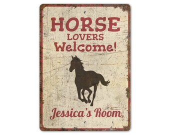 May include: A vintage-style metal sign with a distressed white background and red border. The sign features a silhouette of a horse and the text "Horse Lovers Welcome!" with the name "Jessica's Room" at the bottom.