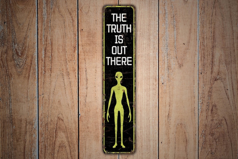 Puede incluir: Un letrero rectangular de metal con el texto "THE TRUTH IS OUT THERE" en letras blancas. Debajo, una figura de alien&iacute;gena verde. El letrero tiene un fondo negro con un aspecto vintage y desgastado. Montado sobre una superficie de madera.