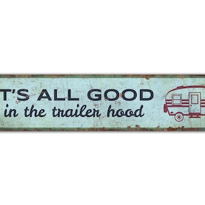 Può includere: Un cartello metallico rettangolare dall'aspetto vintage e usurato. Il cartello ha uno sfondo azzurro chiaro con le parole "IT'S ALL GOOD in the trailer hood" in nero e un'illustrazione rossa di un camper. I bordi sono arrugginiti.