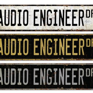 Op de afbeelding: Drie vintage-stijl metalen borden met de tekst "AUDIO ENGINEER DR" in zwarte letters op een witte, zwarte en grijze achtergrond. De borden hebben een verweerde, roestige uitstraling.
