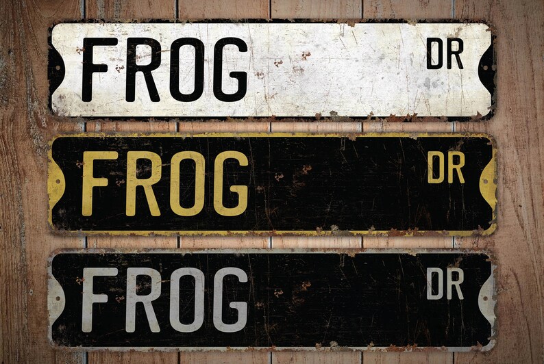 Może przedstawiać: Trzy metalowe tabliczki w stylu vintage z napisem "FROG DR". Tabliczki są w r&oacute;żnych kolorach i mają postarzony wygląd. G&oacute;rna tabliczka jest biała z czarnym napisem, środkowa tabliczka jest czarna z ż&oacute;łtym napisem, a dolna tabliczka jest czarna z białym napisem.
