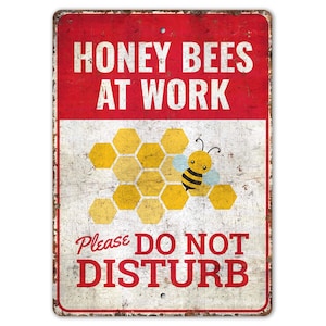 May include: A white metal sign with red text that reads "Honey Bees At Work" and a cartoon bee on a honeycomb. The sign also has the text "Please Do Not Disturb" in red.