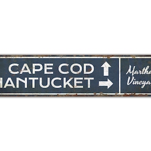 May include: A blue and white metal sign with the text "CAPE COD" and an arrow pointing up, "NANTUCKET" and an arrow pointing right, and "Martha's Vineyard".