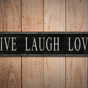 May include: Black wooden sign with white text that reads "LIVE LAUGH LOVE" on a woodgrain background.