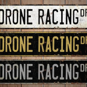 May include: Three vintage-style metal signs with the text "Drone Racing DR" in black, yellow, and white lettering on a black background. The signs have a distressed, rusty look.