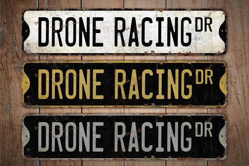 May include: Three vintage-style metal signs with the text "Drone Racing DR" in black, yellow, and white lettering on a black background. The signs have a distressed, rusty look.