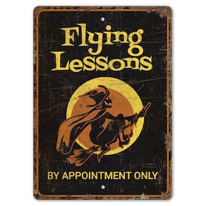 May include: A black metal sign with a distressed finish. The sign features a silhouette of a witch flying on a broomstick in front of a yellow moon. The text on the sign reads "Flying Lessons" and "By Appointment Only".
