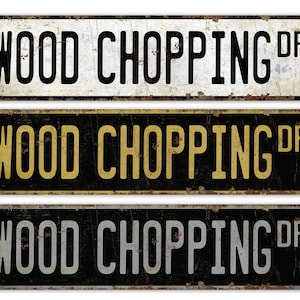 May include: Three vintage-style metal signs with the text "WOOD CHOPPING DR" in black lettering. The top sign has a white background, the middle sign has a black background with gold lettering, and the bottom sign has a black background with silver lettering.