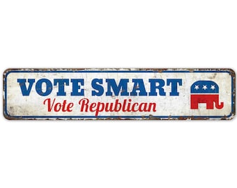 Puede incluir: Un letrero de metal blanco con texto azul y rojo que dice "VOTE SMART Vote Republican". El letrero tiene un elefante rojo, blanco y azul con estrellas en su lado.
