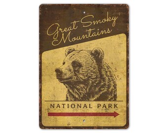 May include: A distressed metal sign with a vintage design. It features a bear illustration and the text "Great Smoky Mountains National Park" with a red arrow. The sign has a brown and yellow colour scheme.
