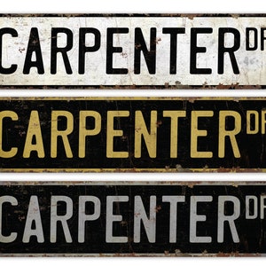 May include: Three vintage-style metal street signs with the text "CARPENTER DR" in black, yellow, and white lettering on a black, white, and black background, respectively. The signs have a distressed, rusty look.