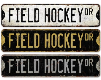 May include: Three vintage-style metal signs with the text "FIELD HOCKEY DR" in black, gold, and silver lettering on a white, black, and black background, respectively.
