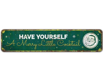 May include: A rectangular, distressed green metal sign with the text "HAVE YOURSELF A Merry Little Cocktail" in white and yellow script. A circular image of Santa Claus is on the right side. The sign has a vintage, rustic aesthetic.