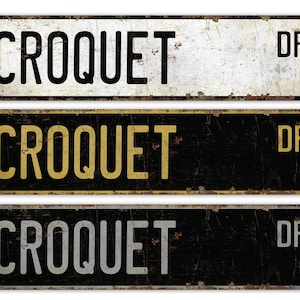 Könnte beinhalten: Drei Vintage-Metallschilder mit dem Text "CROQUET DR" in schwarzer, goldener und silberner Schrift auf schwarzem und weißem Hintergrund.