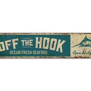 May include: A rectangular metal sign with a distressed finish. The sign features the words "OFF THE HOOK" in white, with "OCEAN FRESH SEAFOOD" below. A blue marlin illustration and the text "Open Daily!" are on the right.