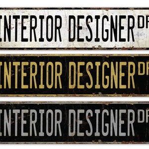 May include: Three vintage-style metal signs with the text "INTERIOR DESIGNER DR" in black lettering on a white, yellow, and gray background. The signs have a distressed, rusty look.