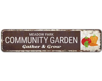 May include: A rusty metal sign with white text that reads "Meadow Park Community Garden Gather & Grow". The sign has a white background with a red tomato, orange bell pepper, and orange carrot.
