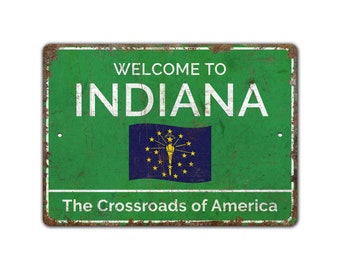Może przedstawiać: Metalowy znak w stylu vintage z zielonym tłem i białym tekstem, który brzmi "Welcome to Indiana The Crossroads of America". Znak zawiera również flagę stanu Indiana z pochodnią i gwiazdami.
