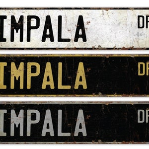Może przedstawiać: Trzy metalowe znaki drogowe w stylu vintage z napisem "IMPALA DR" w czarnych, złotych i białych literach na czarno-białym tle.