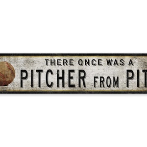 Puede incluir: Un letrero metálico rectangular con un acabado envejecido, con una pelota de béisbol y el texto "THERE ONCE WAS A PITCHER FROM PITT" en letras negras. El letrero tiene una estética vintage y rústica.