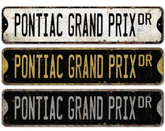 May include: Three vintage-style metal signs with the text "PONTIAC GRAND PRIX DR" in black, gold, and silver lettering on a white, black, and black background, respectively.