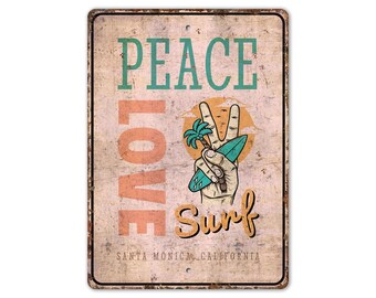 May include: A distressed metal sign with the words "PEACE LOVE SURF". The sign shows a hand making a peace sign, holding a surfboard and palm tree. The text "SANTA MONICA, CALIFORNIA" is at the bottom. The sign has a vintage, weathered appearance.