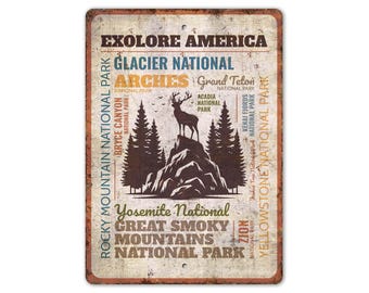 May include: A rectangular metal sign with a distressed finish, featuring the text "EXOLORE AMERICA" and various national park names. A silhouette of a deer stands atop a mountain with pine trees. The sign is a vintage-style travel souvenir.