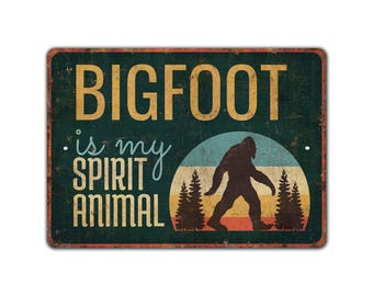 Puede incluir: Un letrero de metal de estilo vintage con fondo verde y una ilustración retro de Bigfoot. El letrero dice "BIGFOOT is my SPIRIT ANIMAL".