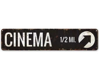 以下が含まれることがあります： 「CINEMA 1/2 MI.」という文字と、円の中に上向きに指し示す白い矢印が描かれた白黒の金属製の標識です。