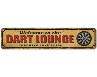 May include: A yellow and brown vintage-style metal sign with the text "Welcome to the Dart Lounge" in red letters and "Throwing Advice: 50¢" in black letters. A dartboard is pictured on the right side of the sign.