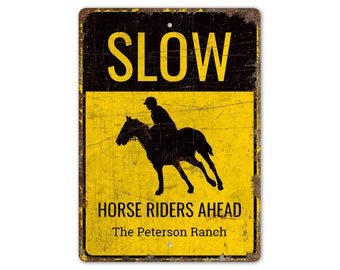 May include: Yellow and black metal sign with the text "SLOW" in large black letters. The sign also features a silhouette of a person riding a horse and the text "HORSE RIDERS AHEAD" and "The Peterson Ranch".