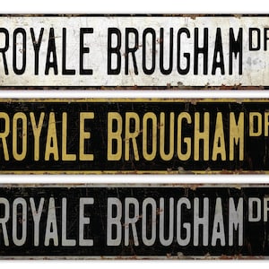May include: Three vintage-style metal signs with the text "Royale Brougham Dr" in black, gold, and silver lettering on a black background.