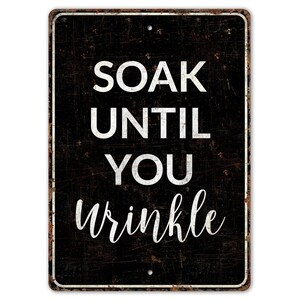 May include: Black metal sign with white text that reads "SOAK UNTIL YOU wrinkle".