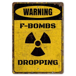 May include: A yellow warning sign with black text and a black radiation symbol. The sign reads "WARNING F-BOMBS DROPPING".