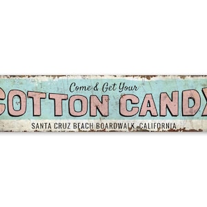 May include: A vintage-style metal sign with a blue and white background. The sign reads "Come & Get Your COTTON CANDY" in pink letters with black outlines. The text "SANTA CRUZ BEACH BOARDWALK, CALIFORNIA" is written in black below the main text.