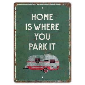 May include: A green metal sign with a distressed look, featuring the text "Home is where you park it" in white. A vintage camper is pictured below the text.