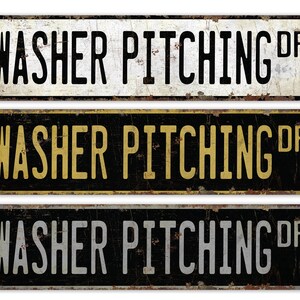 May include: Three vintage-style metal signs with the text "WASHER PITCHING DR" in black lettering. The top sign has white background, the middle sign has a black background with gold lettering, and the bottom sign has a black background with silver lettering.