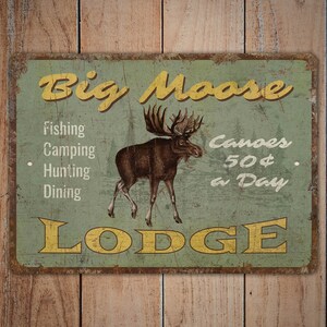 May include: A vintage-style metal sign with a rustic green background and yellow text. The sign reads "Big Moose Lodge" and features a moose illustration. It lists services offered: fishing, camping, hunting, dining, and canoe rentals for $50 a day.