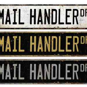 May include: Three vintage-style metal signs with the text "MAIL HANDLER DR" in black lettering. The top sign has a white background, the middle sign has a black background with gold lettering, and the bottom sign has a black background with silver lettering.