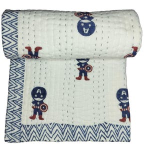 May include: White and blue Captain America quilt. The quilt features a repeating pattern of Captain America figures in red, blue, and white. The border has a blue and white zigzag design. The quilt is rolled up at the top.