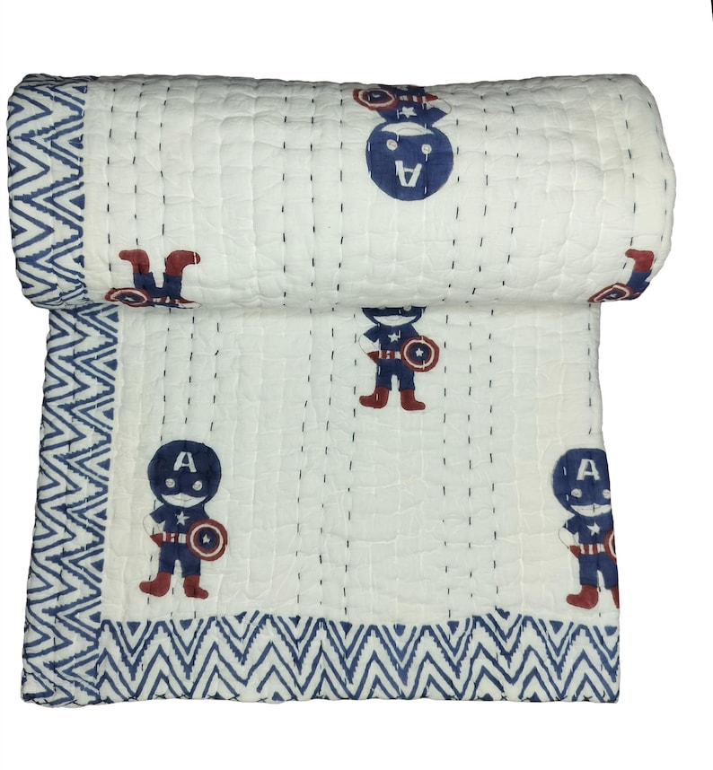 May include: White and blue Captain America quilt. The quilt features a repeating pattern of Captain America figures in red, blue, and white. The border has a blue and white zigzag design. The quilt is rolled up at the top.