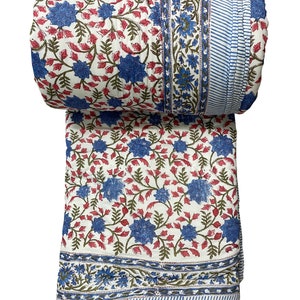 Op de afbeelding: Een wit katoenen dekbed met een bloemenpatroon in tinten blauw, rood en groen. Het dekbed is opgerold en heeft een blauw-wit gestreepte rand.